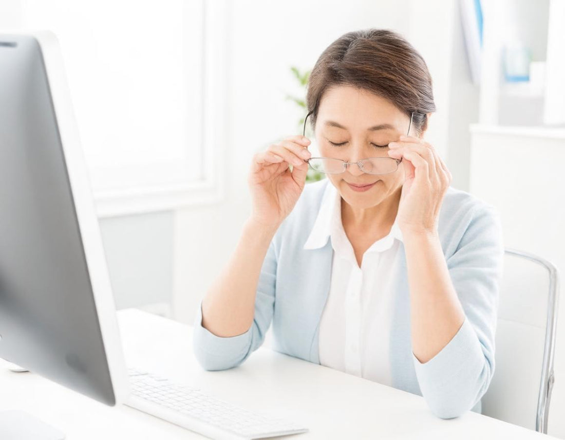 Woman at a computer lifting her glasses and resting her tired eyes
