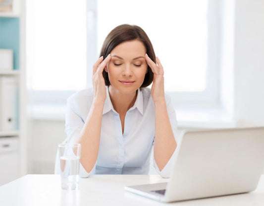Woman at a desk gently pressing her temples to relieve a tension headache